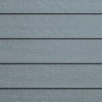 Close-up of gray horizontal wooden siding panels, showing a textured, wood grain pattern. The boards are evenly spaced, creating a repeating linear design across the surface.