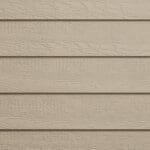 Close-up of beige horizontal wood siding on a building exterior, showing the textured grain pattern and slight shadows between each plank.