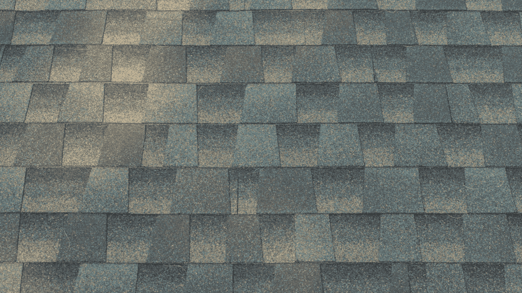 Close-up view of a roof covered in gray asphalt shingles arranged in a uniform pattern. The shingles have a textured surface and subtle variations in color, creating a checkered appearance under natural light.