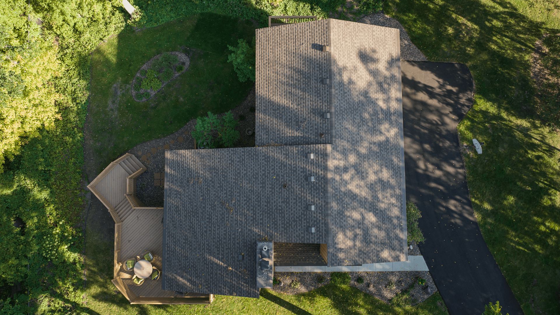 Aerial view of a completed dark architectural shingle roof on a residential home with mature trees casting shadows