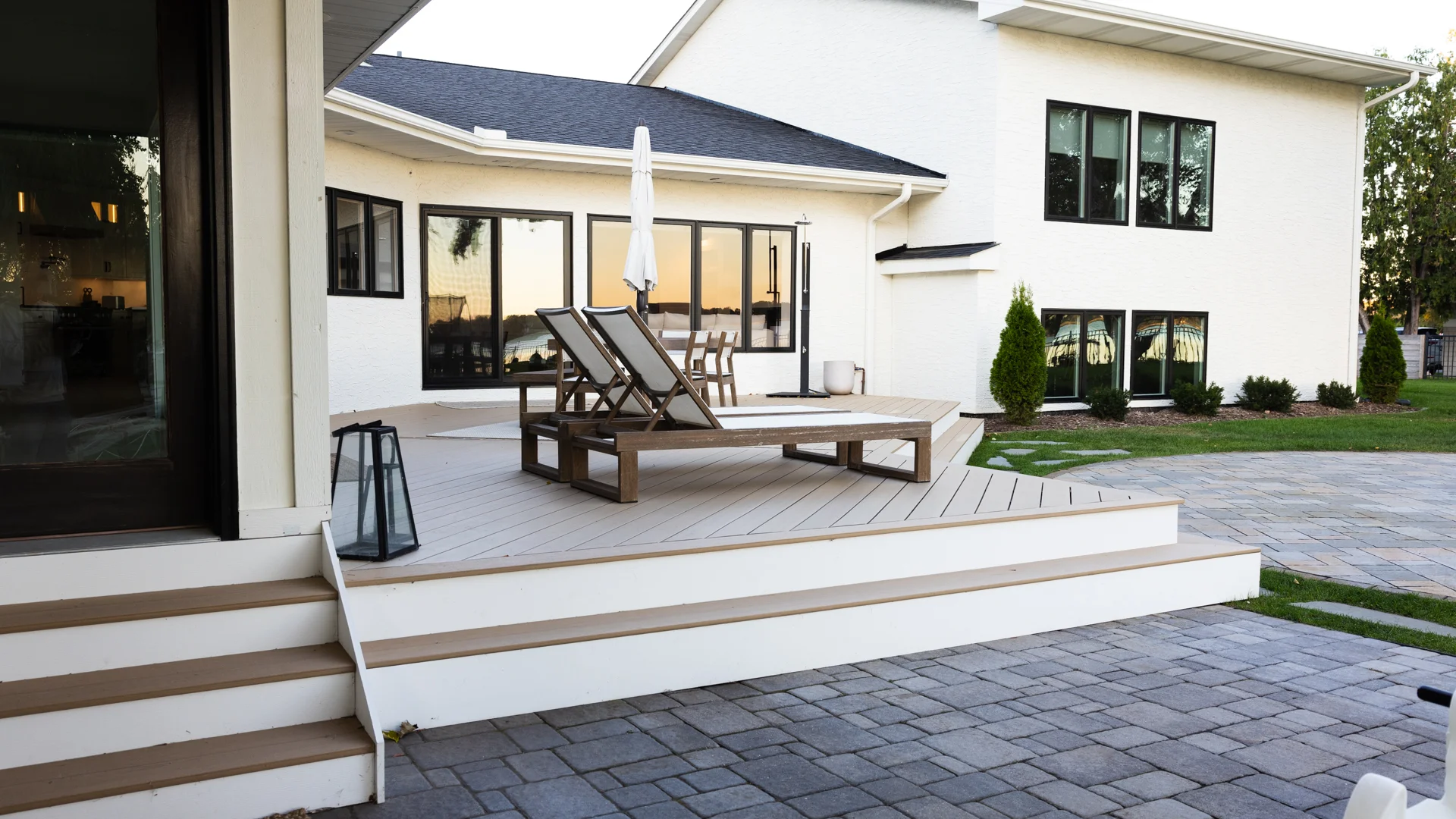 Modern residential exterior with composite deck, patio pavers, and new black-framed windows on white siding