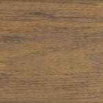 Close-up of a wooden surface with a natural brown color and visible grain patterns. The texture looks slightly rough, with subtle variations in tone and horizontal lines.
