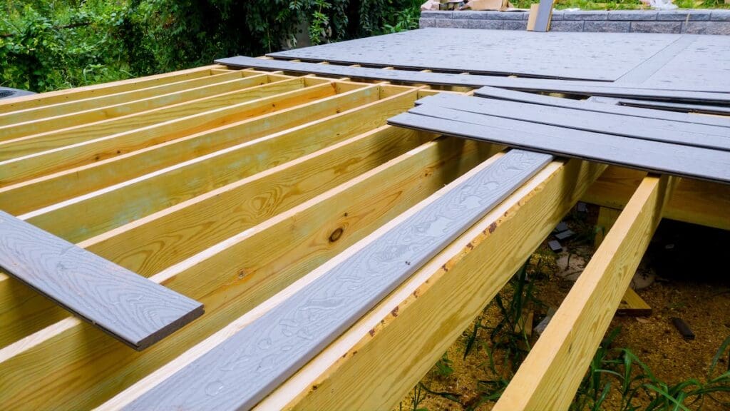 Partially constructed wooden deck frame with gray composite deck boards being installed on top