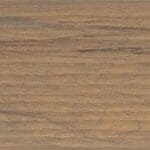 A close-up view of a wooden surface showing natural grain patterns and varying shades of brown and tan with subtle hints of darker streaks.