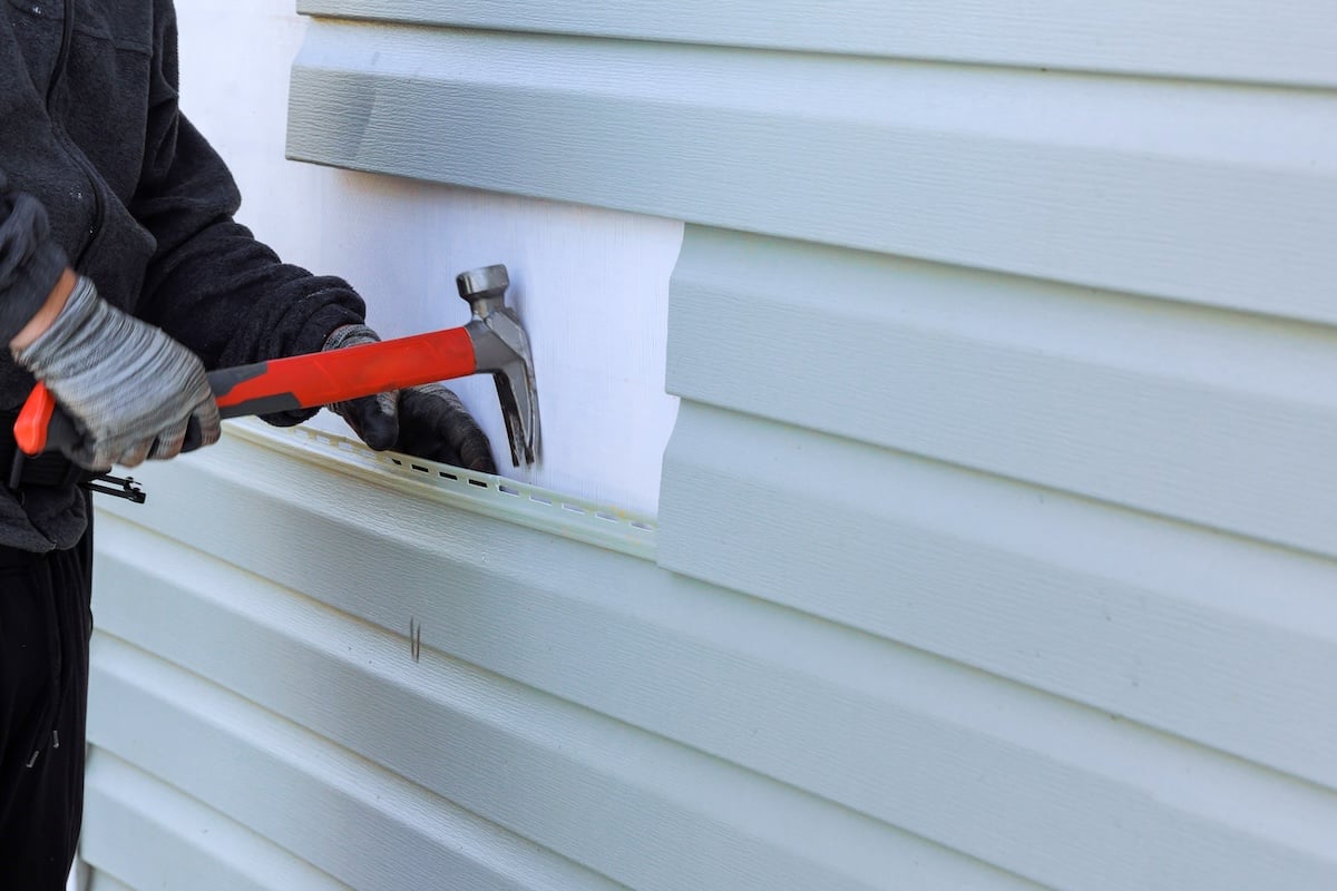 Worker using a hammer to remove vinyl siding