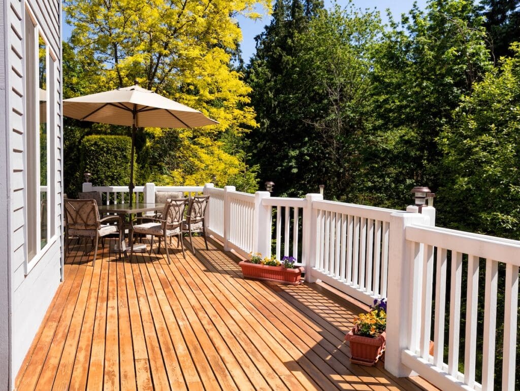 A spacious wooden deck with white railings and cedar decking boards features a table, chairs, and a large umbrella.