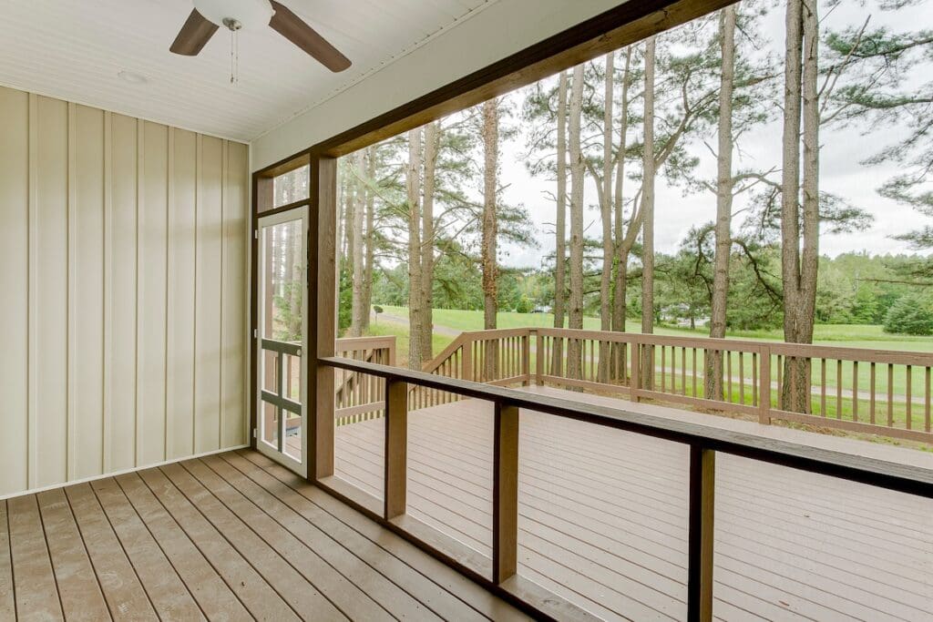 A screened-in porch with wood flooring and railing overlooks a spacious and a scenic view of tall pine trees