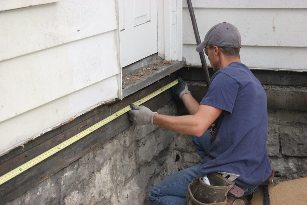 A person measures the lower edge of a house exterior with a tape measure