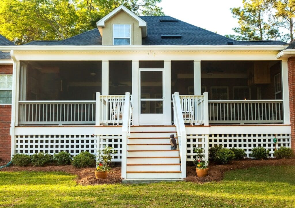 A screened-in porch with white railings and stairs leads to a lawn