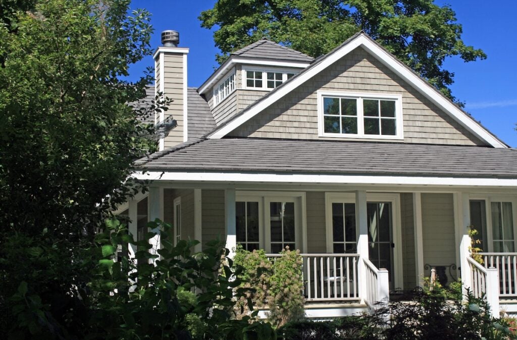 A beige house with shingle siding and white trim features a covered front porch