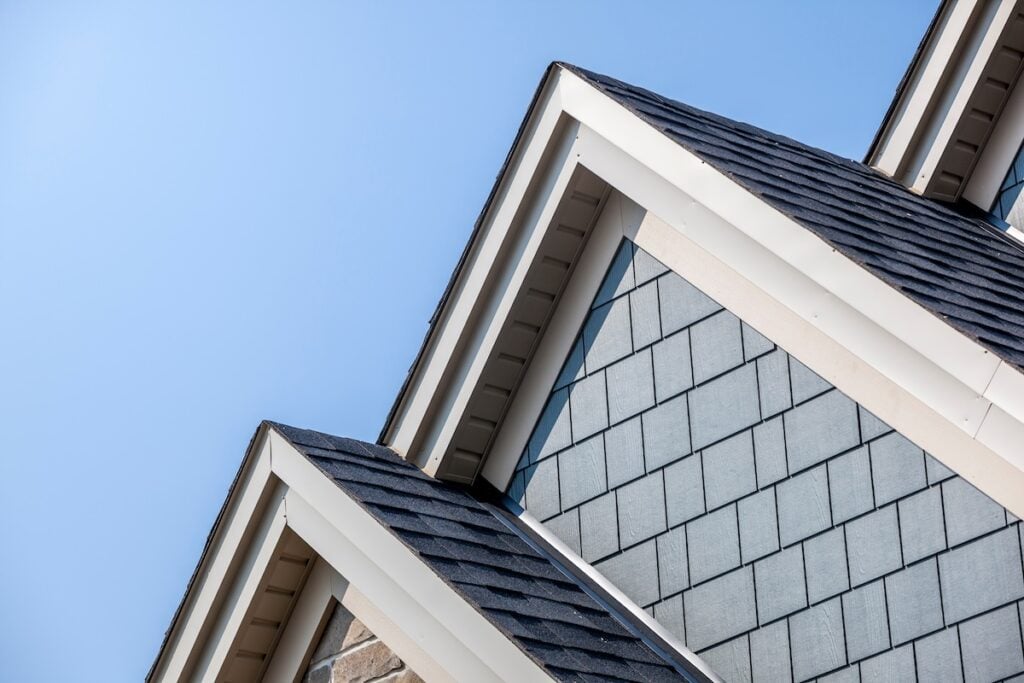 Close-up view of house dormers with dark asphalt shingles and muted blue shaker siding