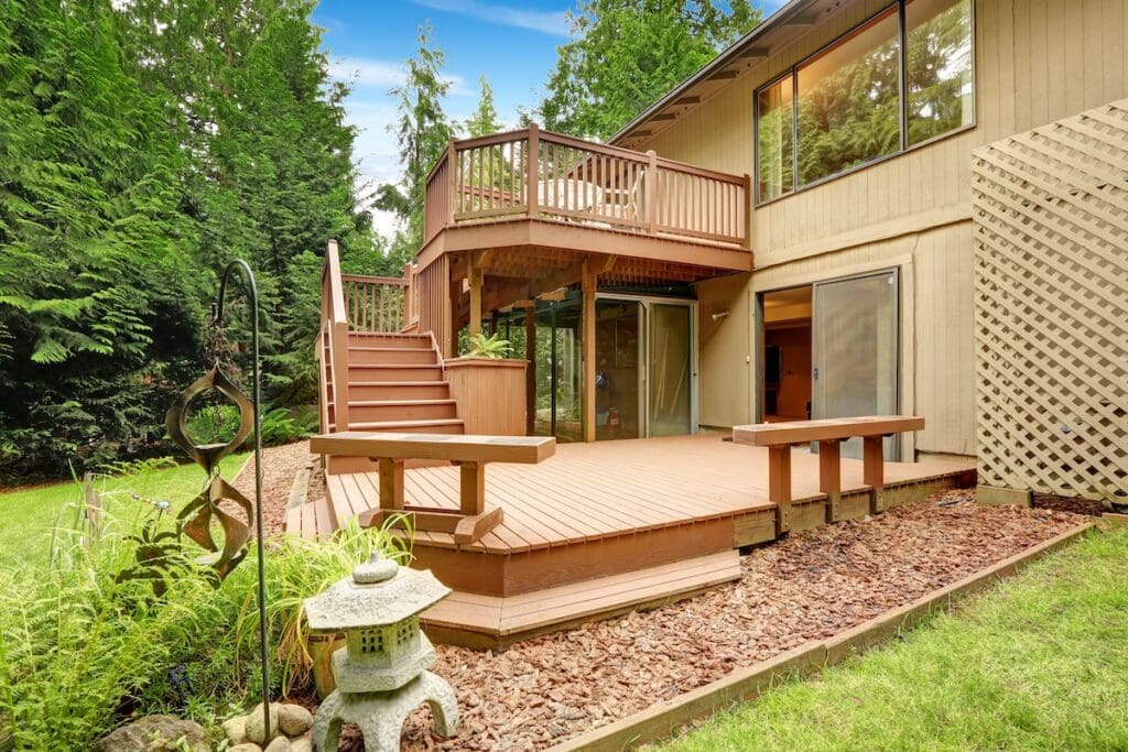 Spacious backyard with a multi level deck featuring benches and stairs, surrounded by lush green trees and shrubs