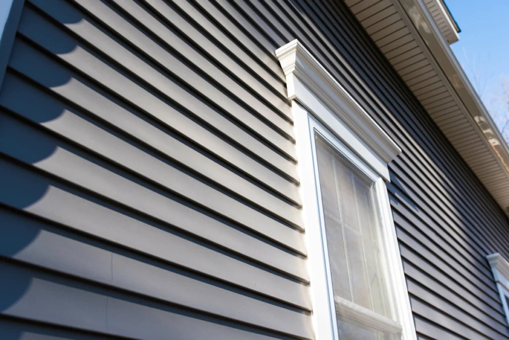 Close-up view of gray siding Arden Hills on a house exterior, featuring a white-trimmed window and roof eaves, all shown on a sunny day.