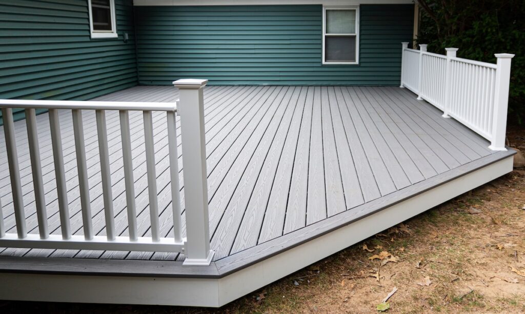 New composite deck on the back of a house with green vinyl siding.with white railings.