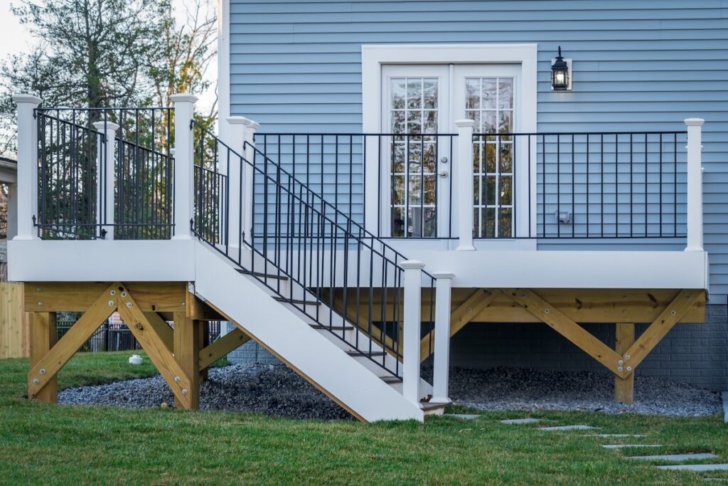 A newly built wooden deck with white railings and black balusters, attached to a blue house