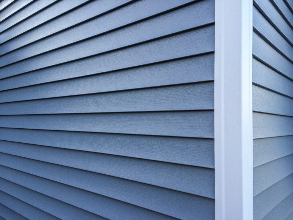 Close-up view of the exterior corner of a building with blue horizontal weatherproof siding and a white vertical trim piece, showing clean, neat lines and smooth textures.