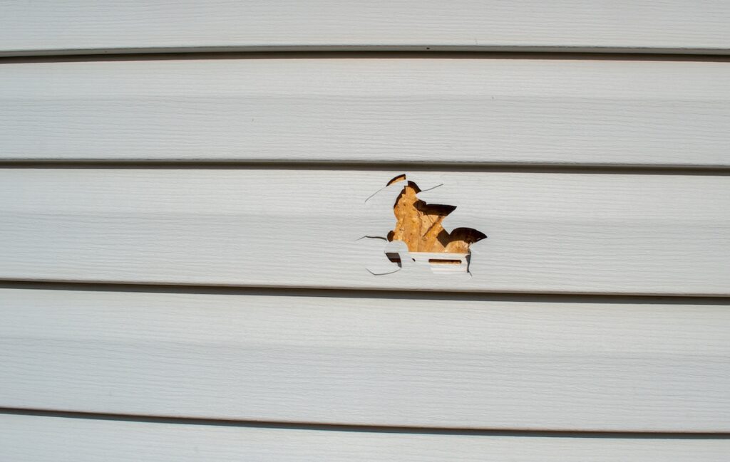 A lawnmower and a rock resulted in a punctured piece of vinyl siding on this home. Siding replacement professionals may be hired soon.