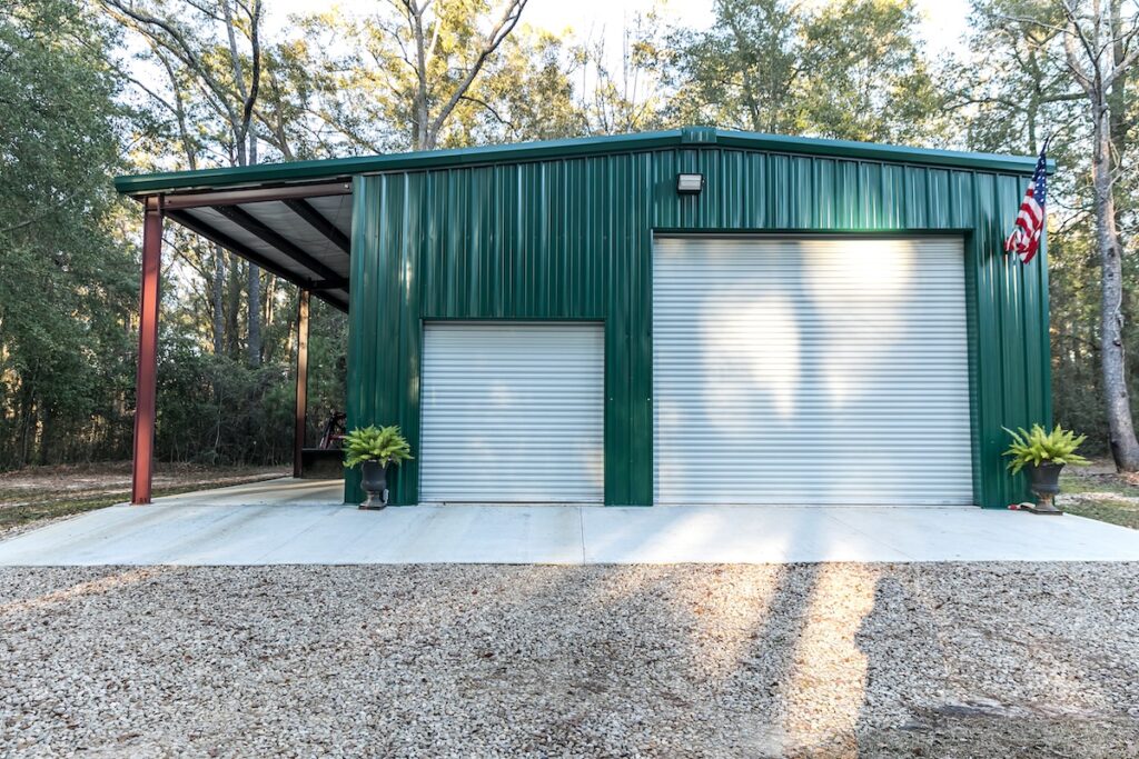 A green metal building with two large roll-up garage doors