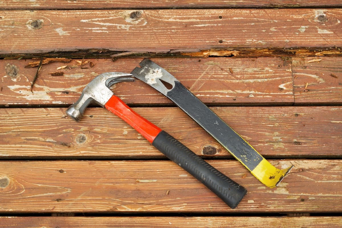 Horizontal photo of old hammer and pry bar next to rotting wood on cedar wooden deck