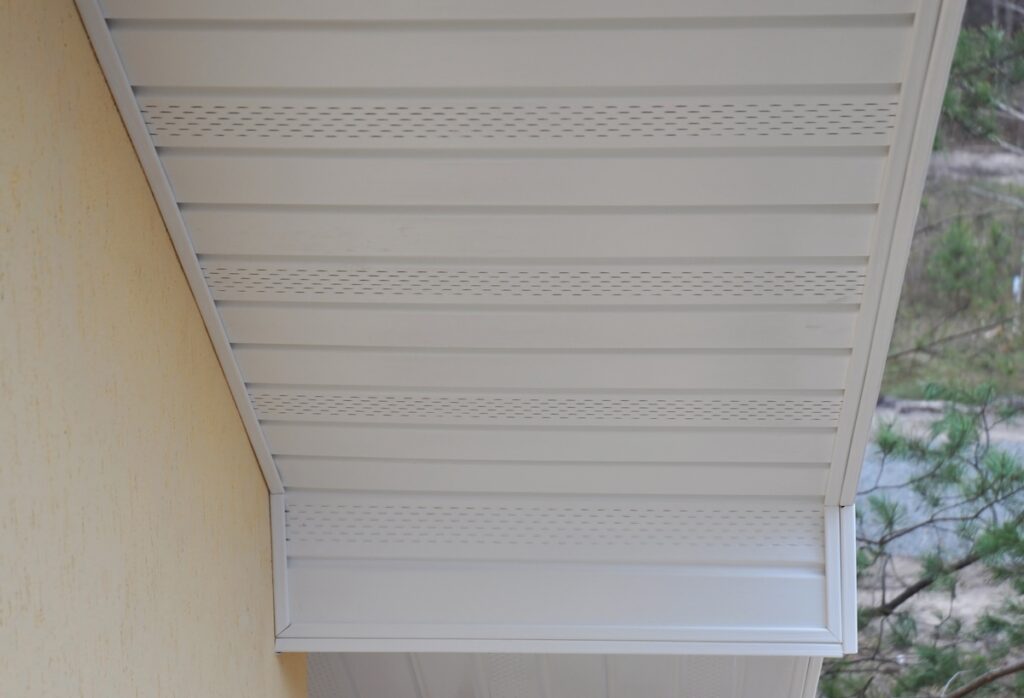 Close-up view of white soffit panels under the edge of a Plastic white uPVC soffit board below the facia of the roof.