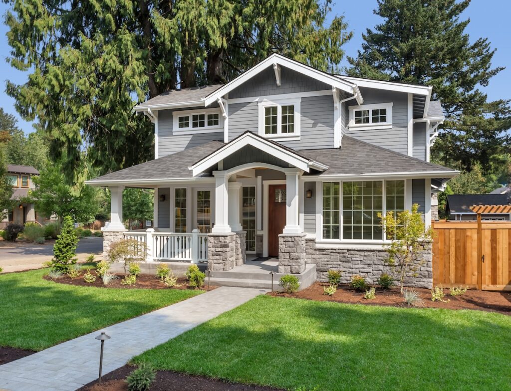 A two-story gray house with white trim, large windows, a covered front porch, and well-maintained landscaping showcases easy vinyl siding maintenance, all set under sunny skies.