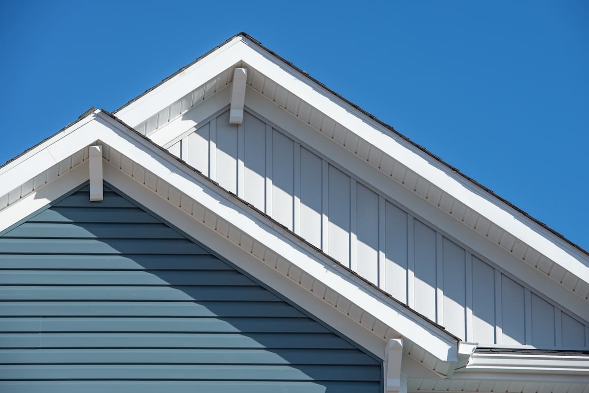 Close-up of the exterior of a house featuring two gabled roofs, showcasing quality siding with blue horizontal panels and white vertical siding, all under a clear blue sky.