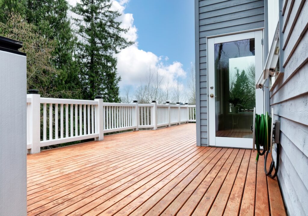 Spacious wooden deck with white railing attached to a gray house