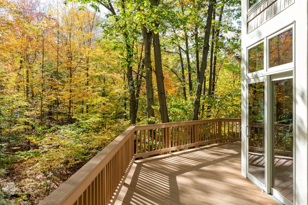 A wooden deck with a railing overlooks a lush forest with colorful autumn foliage.