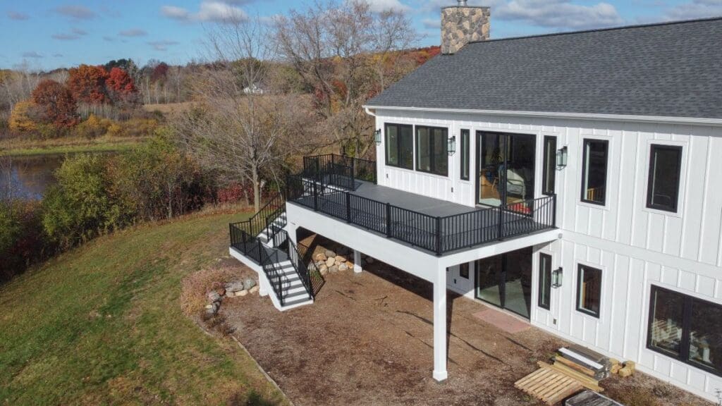 A modern white house with large windows has a raised black metal deck