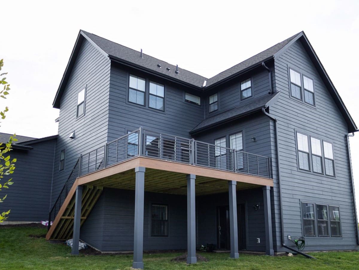 A modern two-story house with a raised wooden deck with metal railings