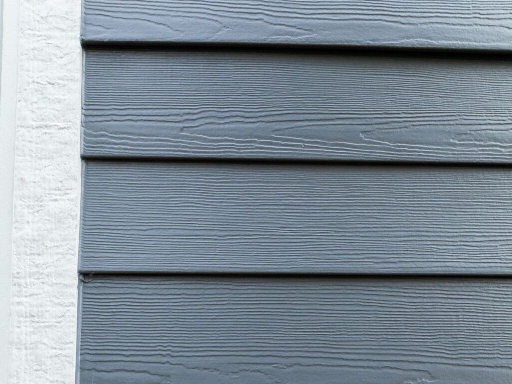 Close-up of gray horizontal siding with a wood grain texture alongside a vertical strip of white textured wall, highlighting the clean lines and the role of quality siding underlayment for added protection.