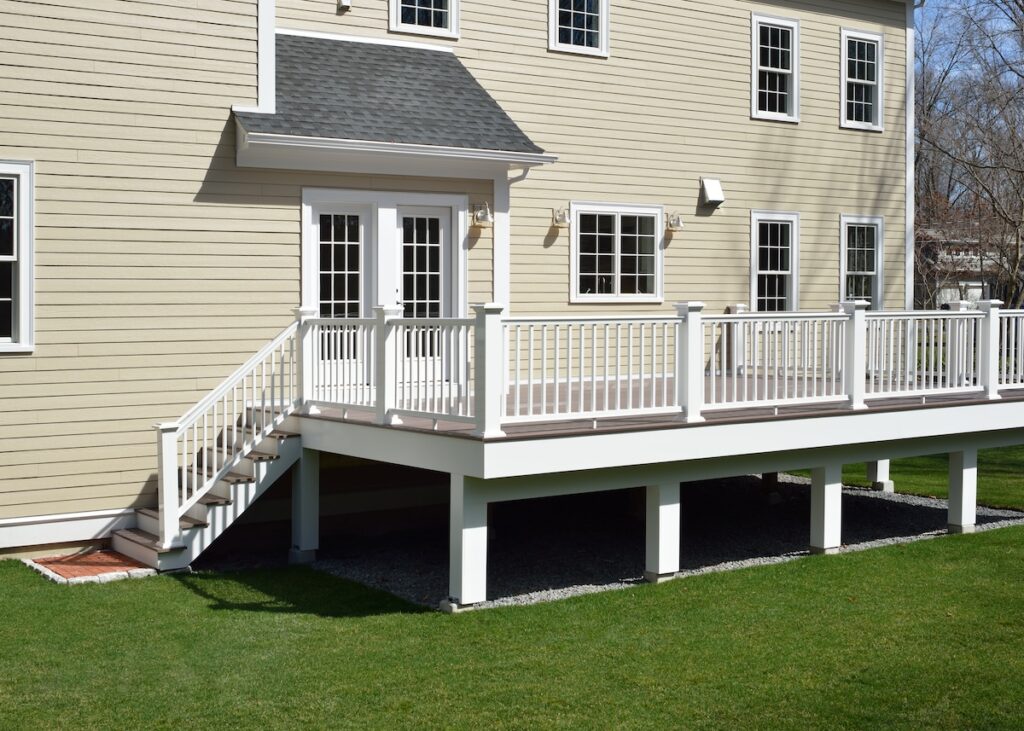 A beige house with white trim features a raised wooden deck with white railings