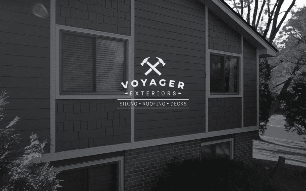 A house exterior with large windows and wood siding; the logo "Voyager Exteriors," trusted Twin Cities siding contractor, with crossed hammers and the text "Siding • Roofing • Decks" appears centered over the image.
