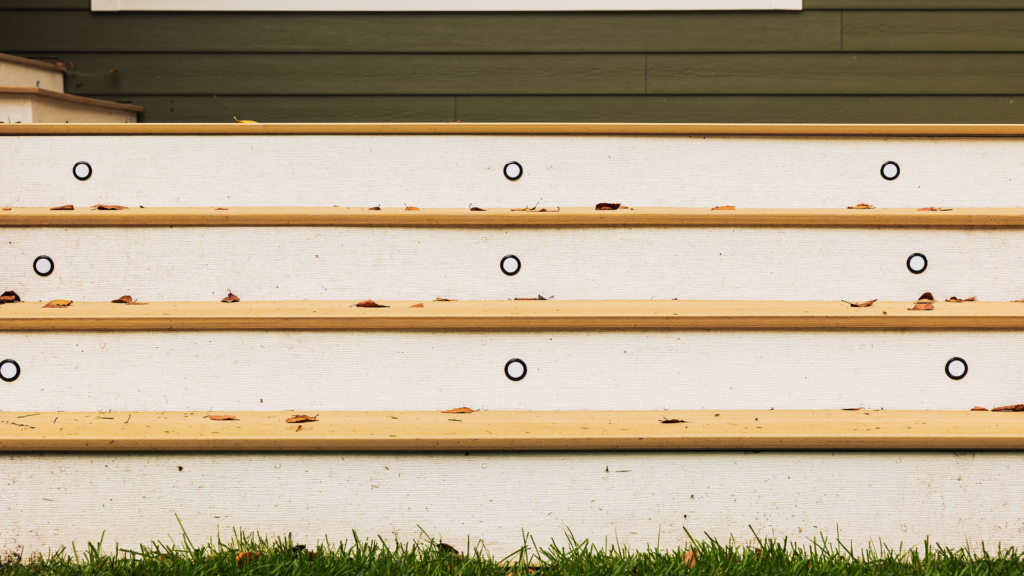 Close-up of outdoor wooden steps with Timber Tech Cypress treads and white risers. Deck stair riser lights, integrated LED riser lighting on composite deck steps.