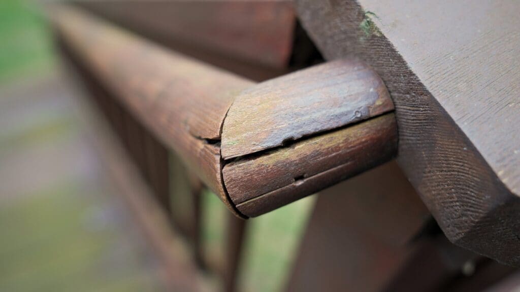Close-up of a cracked and weathered wooden handrail, showing signs of aging and damage—a clear indicator of when to replace a deck. Blurred background highlights the need for expert help from a Twin Cities deck contractor.
