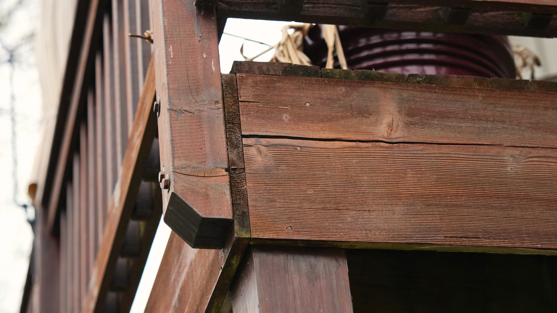 Close-up of weathered wooden railing and support beams on an outdoor staircase, with a large maroon planter and dried plants visible—highlighting where Twin Cities homeowners might need exterior repair services.