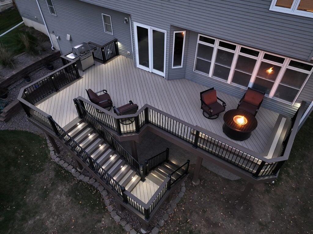 Aerial view of a modern backyard deck at dusk, featuring outdoor seating, a fire pit, and illuminated stairs. Perfect inspiration if you're wondering when to replace a deck or need advice from a trusted Twin Cities deck contractor.