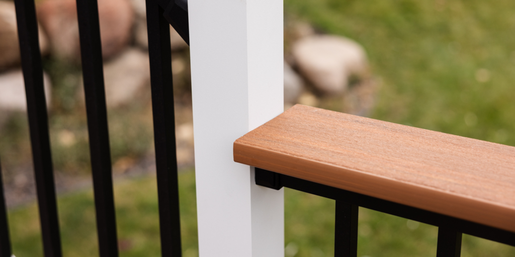 Close-up of a deck railing corner with a white vertical post, black metal balusters, and a brown wooden or composite handrail—an inspiring example for composite railing ideas and perfect for adding drink rails to your outdoor space.