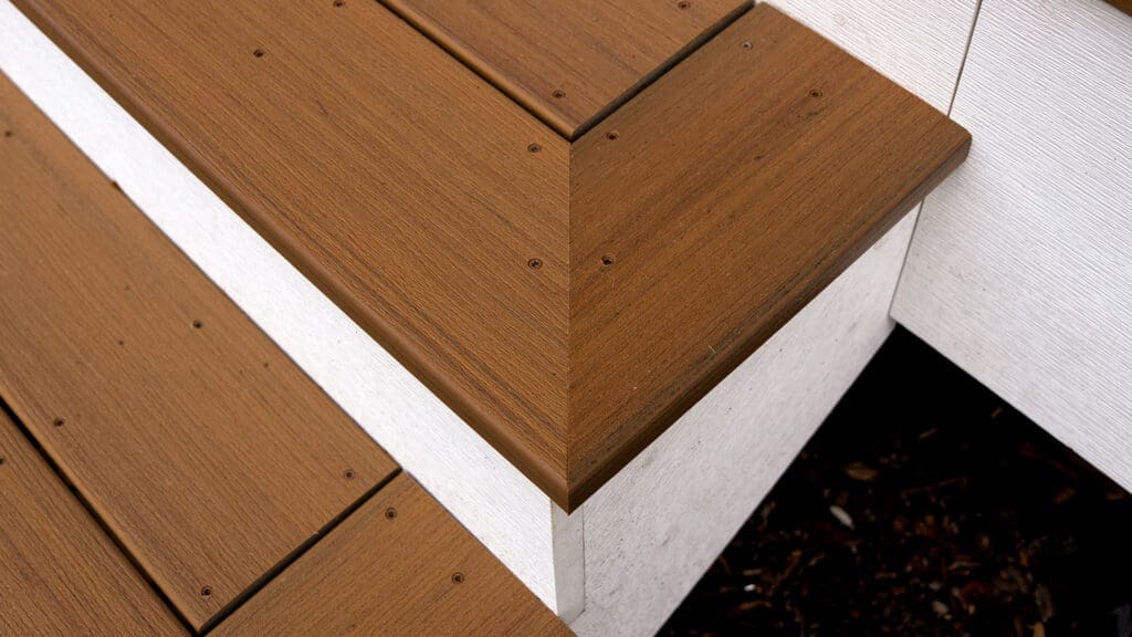 Close-up of a wooden step corner with neatly aligned TimberTech White Oak deck boards and white risers, showcasing precise craftsmanship and clean edges—perfect for siding and deck installation in Coon Rapids MN.
