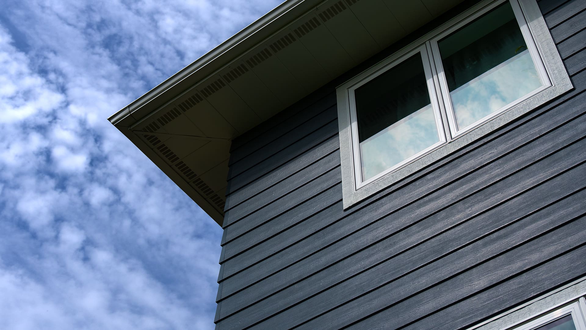Completed fibre-cement horizontal siding in charcoal grey on a residential home with white trim windows