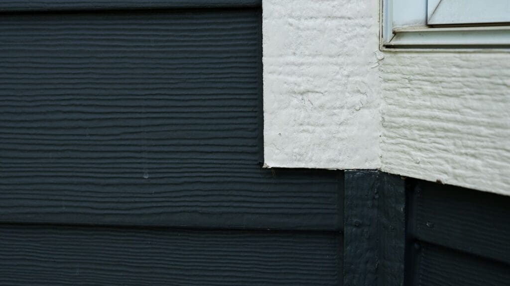 Close-up of the corner of a building exterior shows dark horizontal wood siding meeting textured off-white stucco near a window frame, highlighting details often checked for Minnesota hail damage siding.