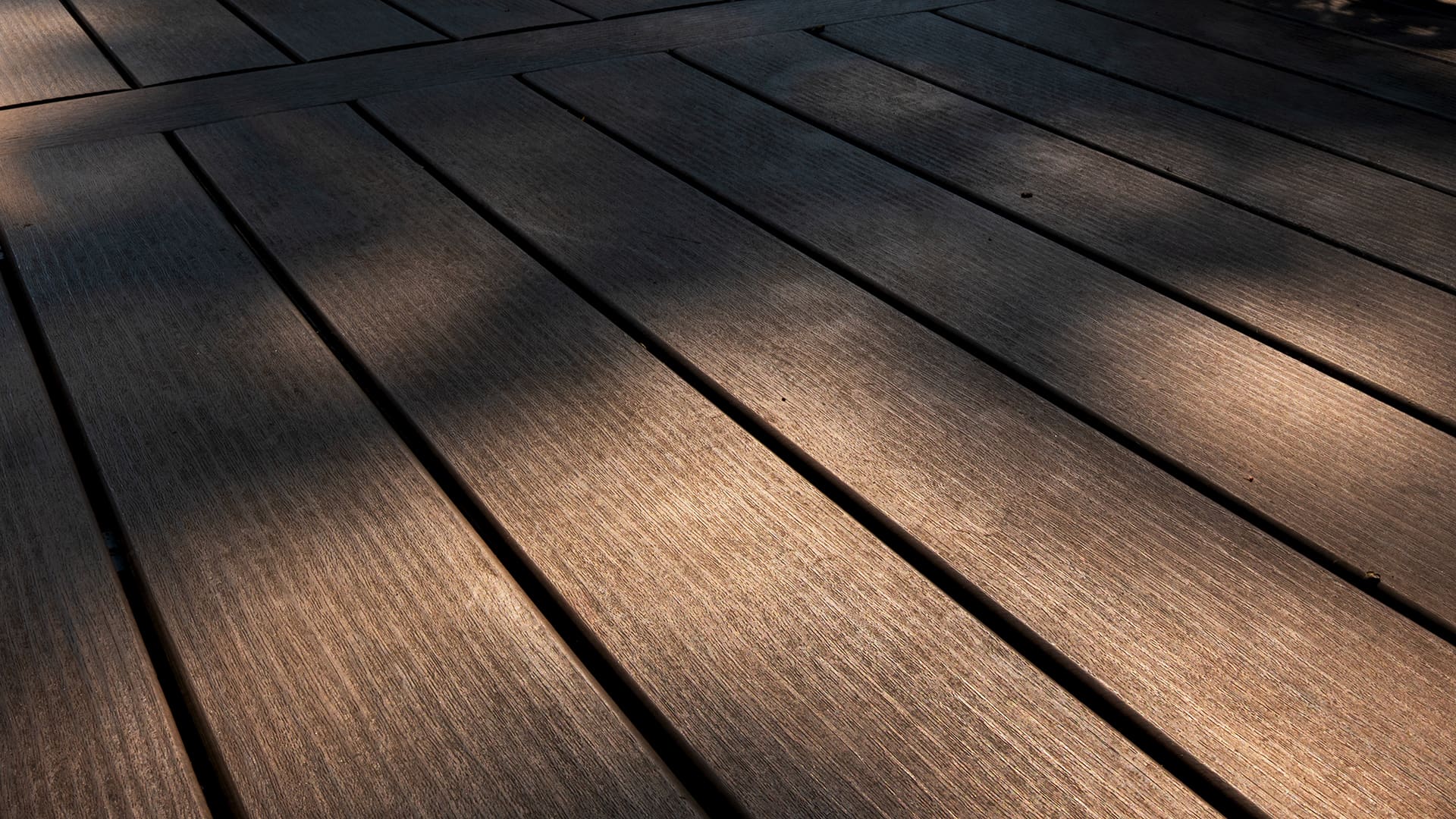 Sunlight and shadows fall across a wooden deck with wide, evenly spaced planks, creating a warm and textured pattern on the surface—an inviting showcase of the craftsmanship found in decks Andover homeowners admire.