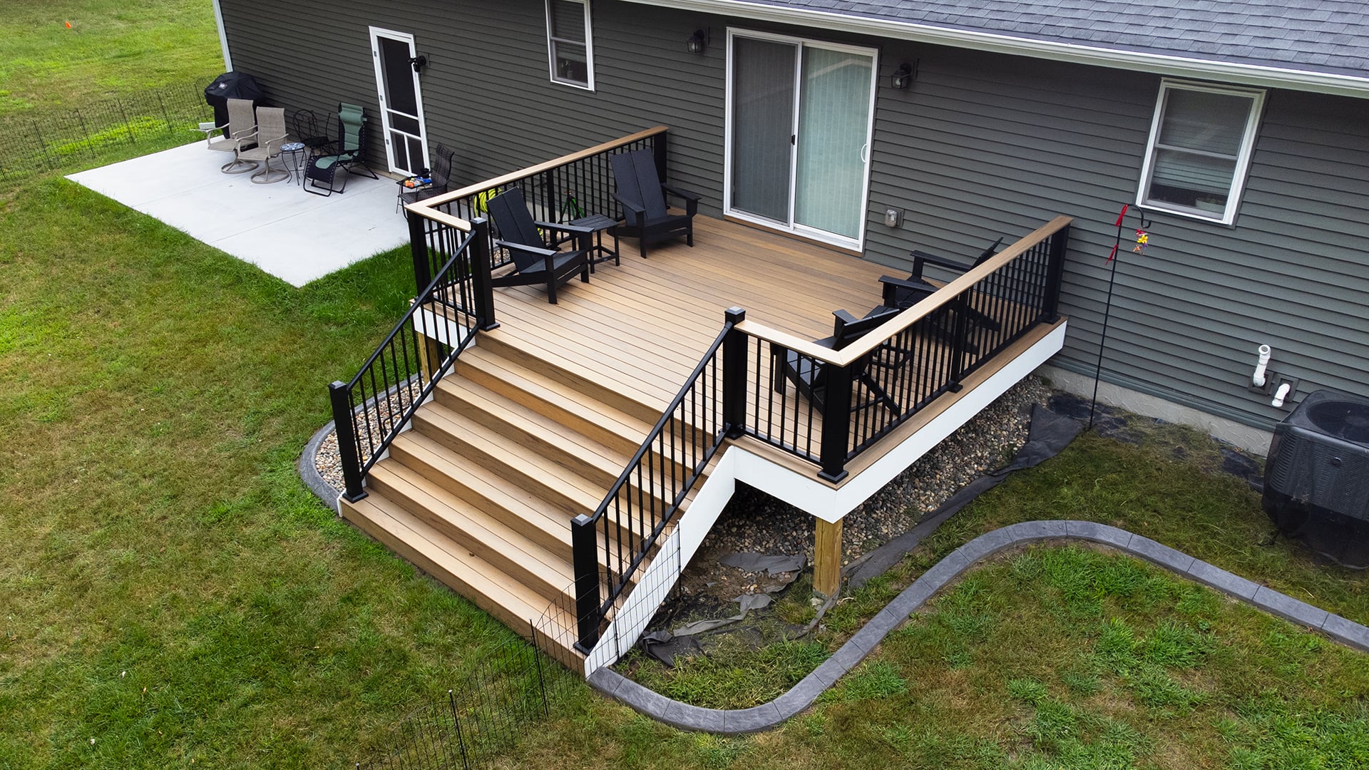 An elevated TimberTech composite deck in Dark Cocoa with stairs and black railings leading down to a concrete patio and backyard.