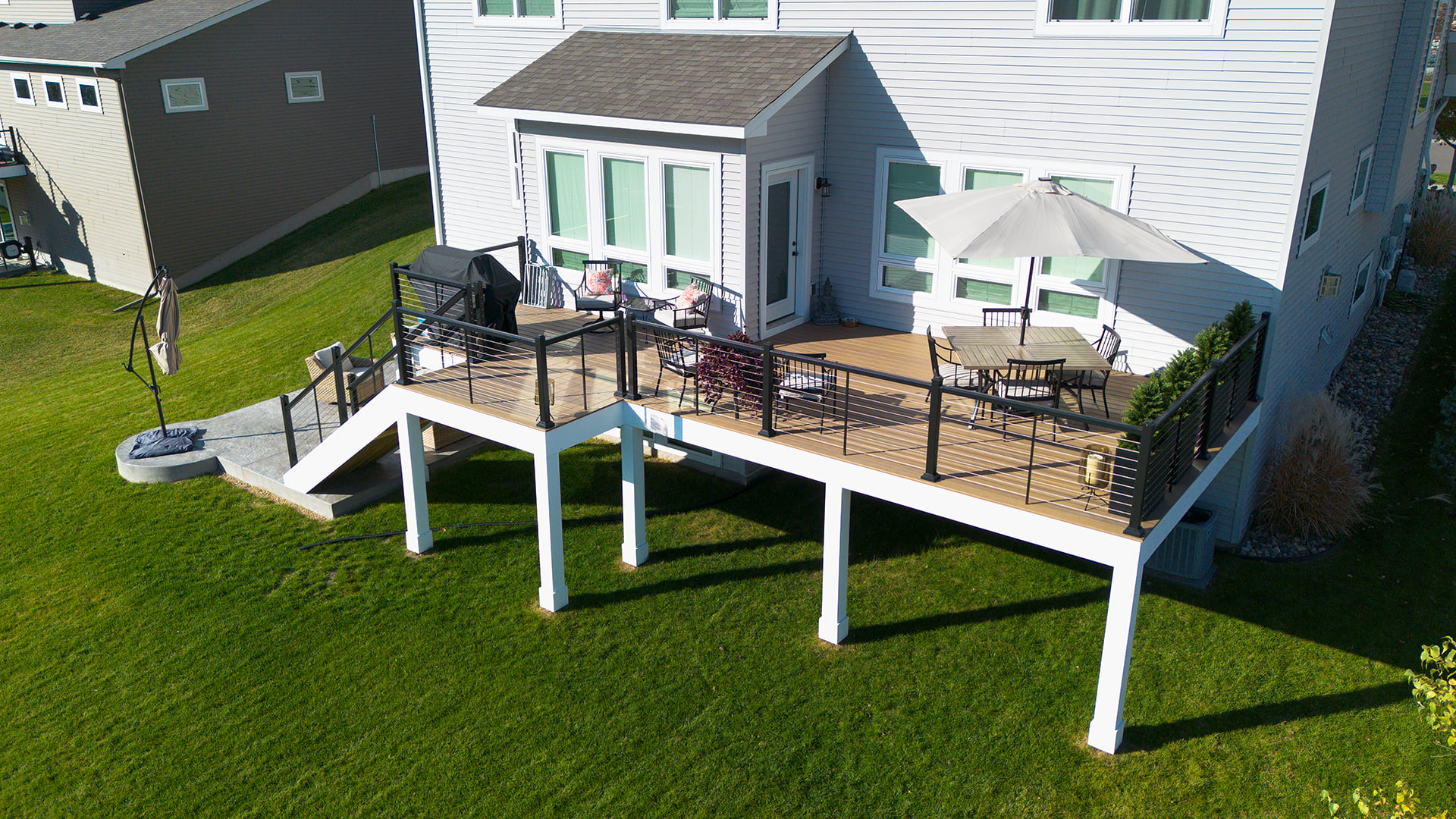 An elevated TimberTech deck in Vadnais Heights featuring a dining set, umbrella, and grill, with stairs leading down to a lawn.